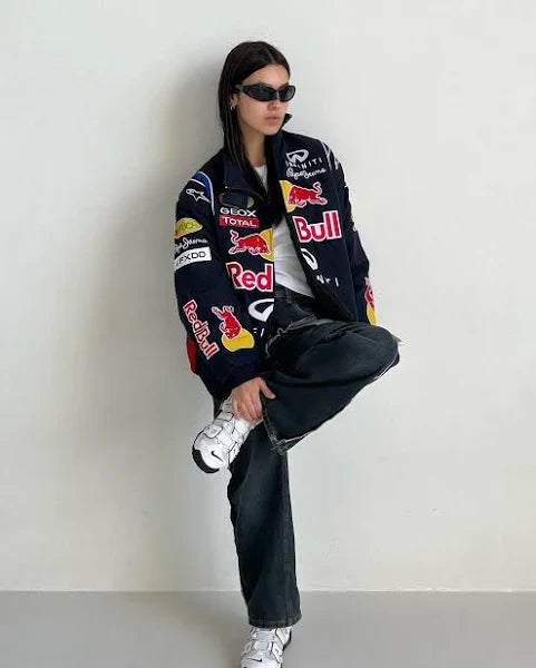 Streetwear model walking in urban space wearing a Red Bull Racing oversized jacket and wide-leg jeans